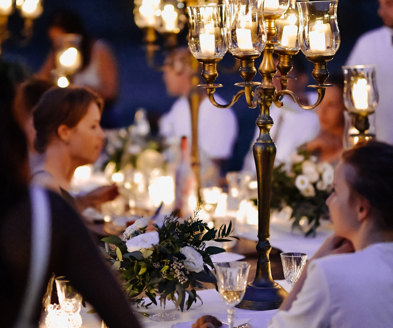 Decorated tables with floral composition and old fashioned candlesticks and guests in the celebration evening