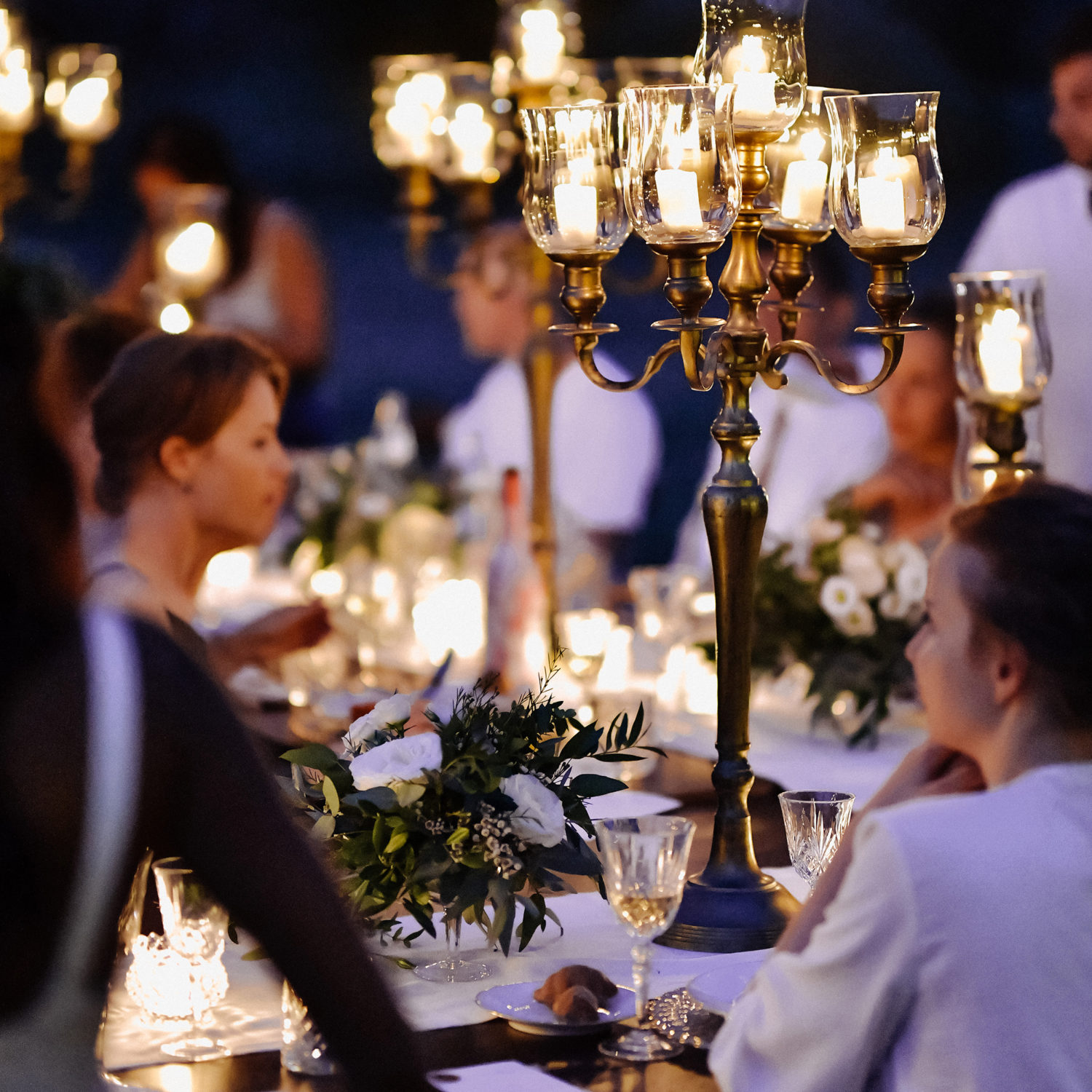 Decorated tables with floral composition and old fashioned candlesticks and guests in the celebration evening